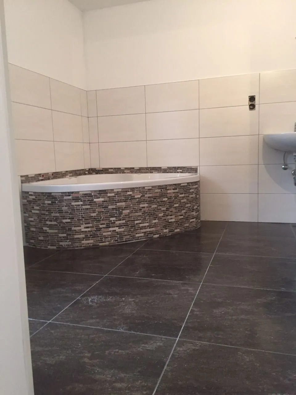 Badewanne mit Mosaikverkleidung vor hellen Wandfliesen