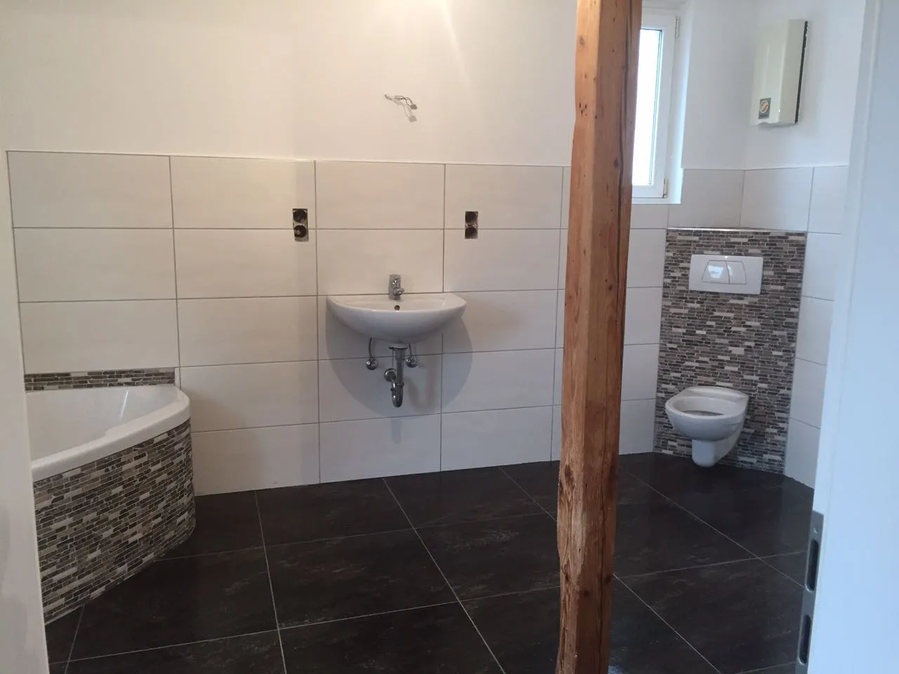Fertiges Badezimmer mit weißen Wandfliesen, dunklem Boden und Mosaikakzenten