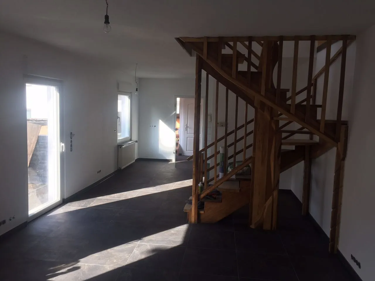 Wohnraum mit großformatigem anthrazitfarbenem Fliesenboden und Holztreppe