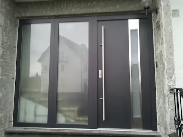 Dunkle Haustür mit zwei Glas-Seitenteilen in einer Natursteinfassade