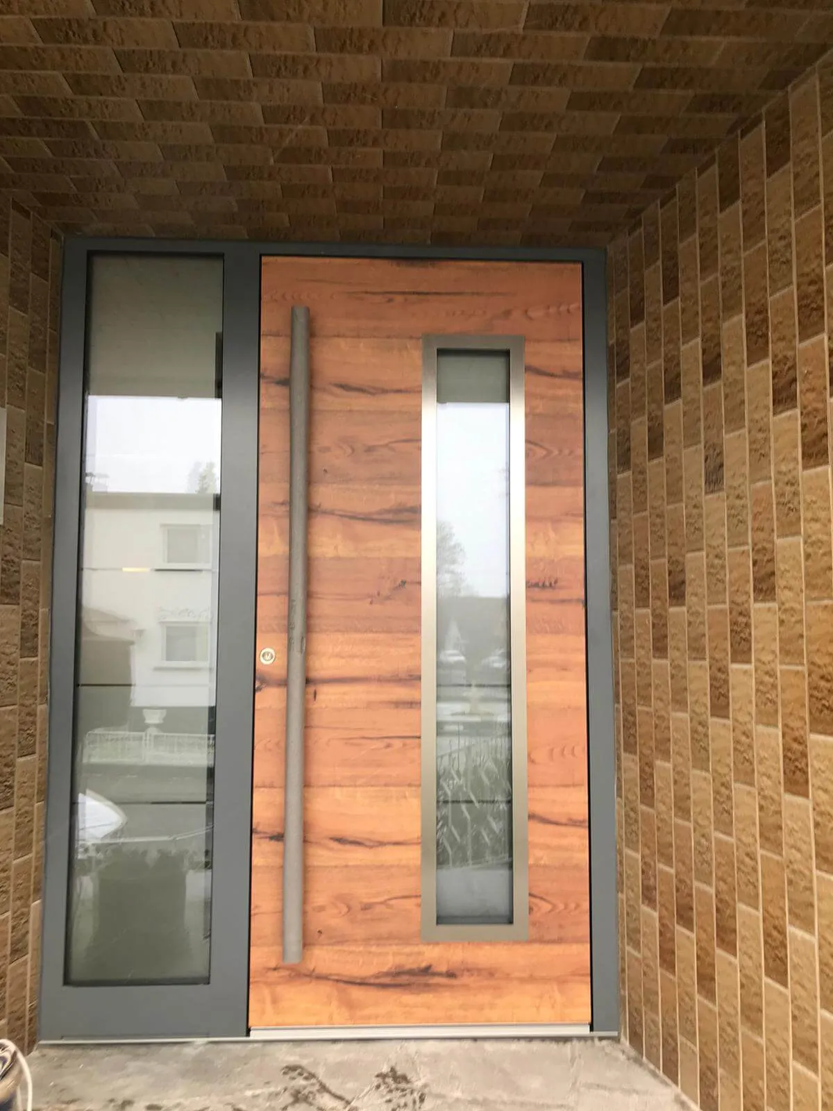 Neue Haustür in Holzoptik mit Aluminiumrahmen und langer Griffstange nach dem Austausch