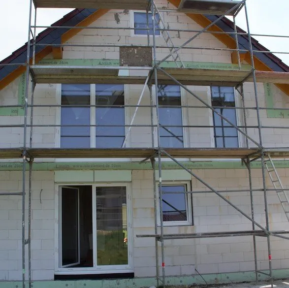 Neubaufassade mit eingesetzten Fenstern und angebrachter Außendämmung, Gerüst davor