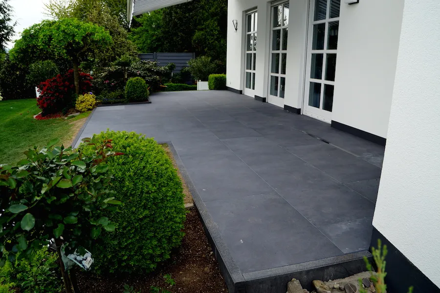 Terrasse mit anthrazitfarbenen Natursteinplatten entlang einer weißen Hausfassade
